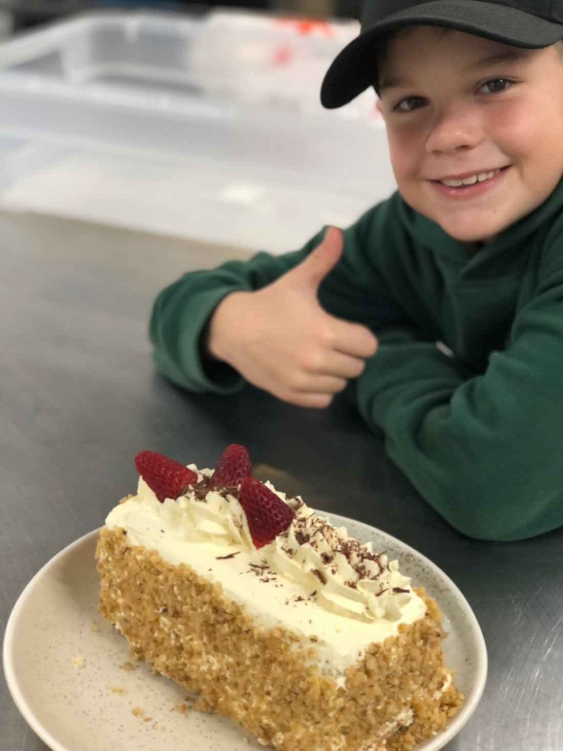A smiling child giving a thumbs up beside a slice of cake.