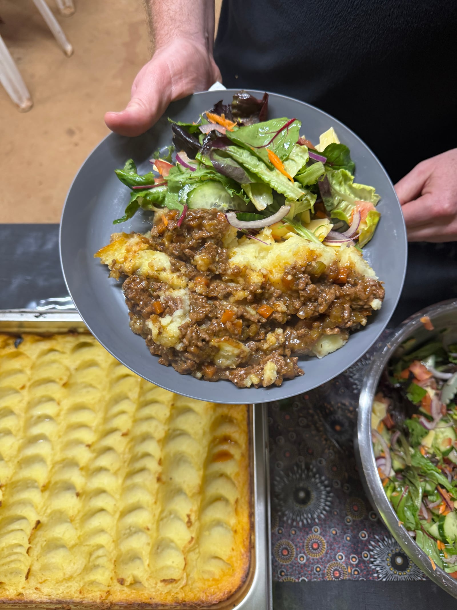 A plate of shepherd's pie with fresh salad at a catered meal.