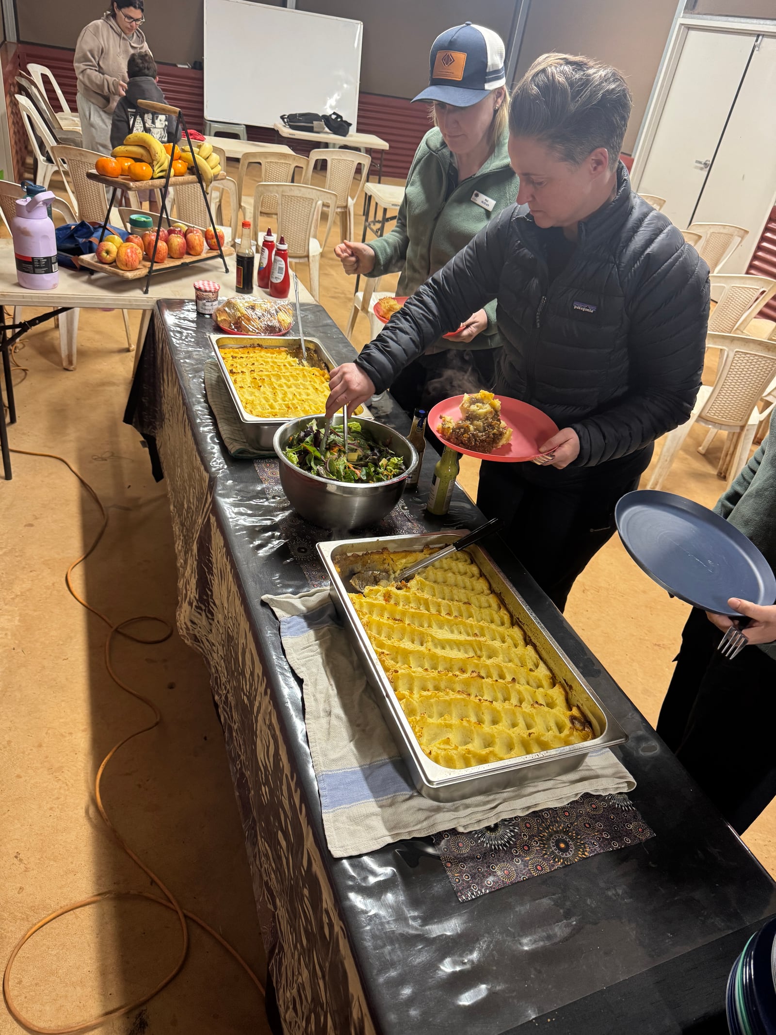 Guests serving shepherd's pie and salad from a buffet table.