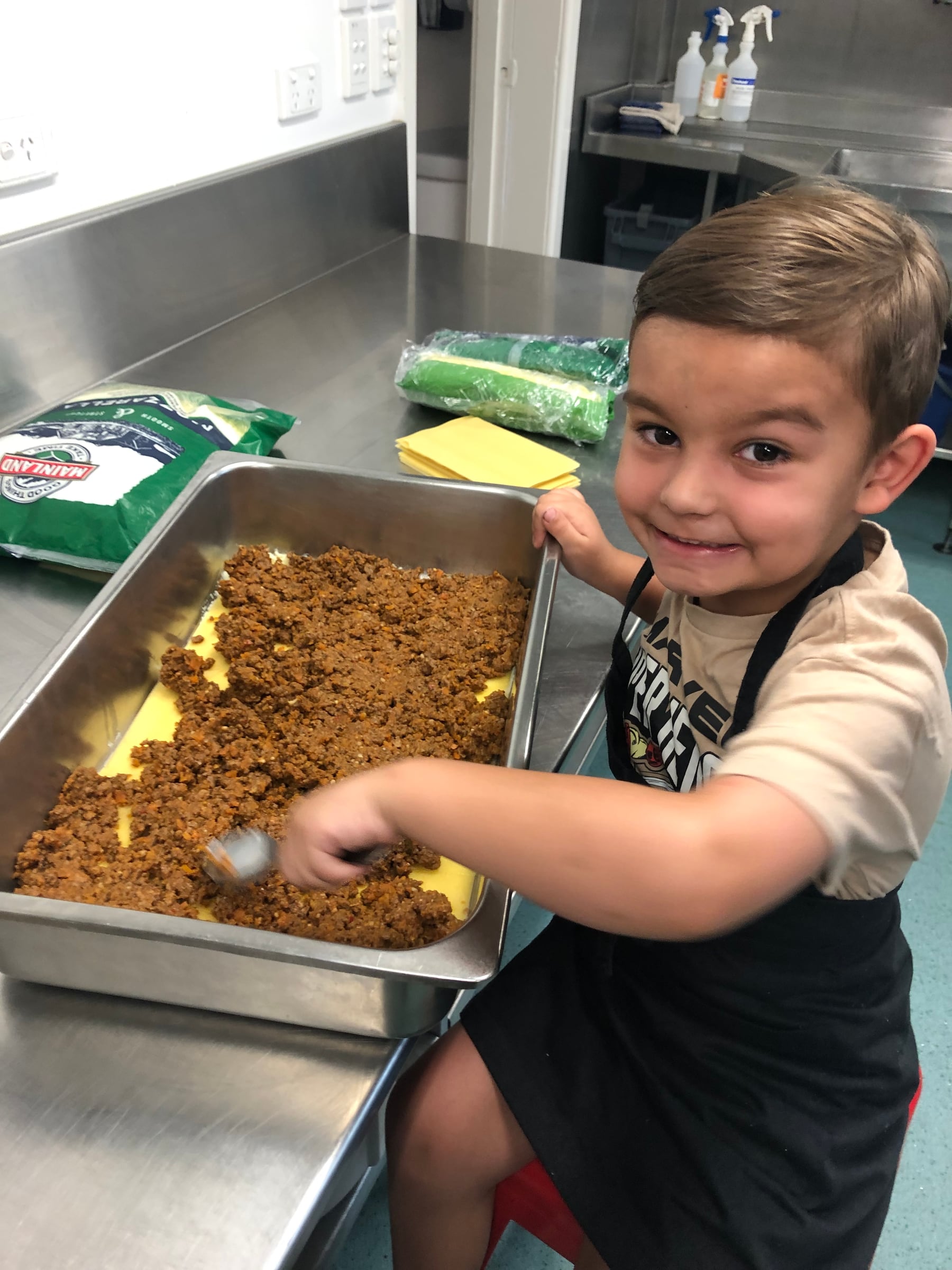 A young helper preparing a tray of lasagne in the kitchen.