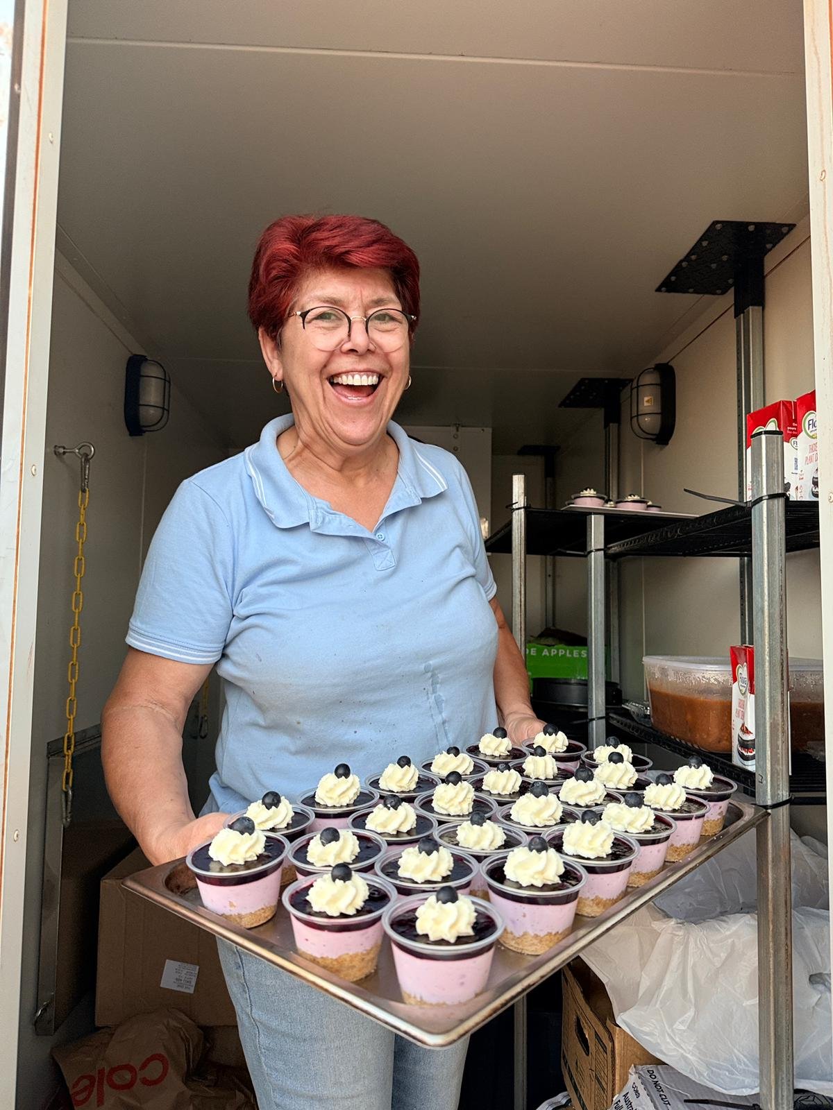 Aunty Donna beaming in her food trailer, holding a tray of fresh mini cheesecakes.